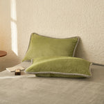 Deux oreillers verts texturés reposent sur une surface blanche près d'un petit objet noir.