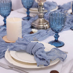 Une table élégante avec des verres bleus, des bougies et une nappe grise, créant une ambiance raffinée et sophistiquée.