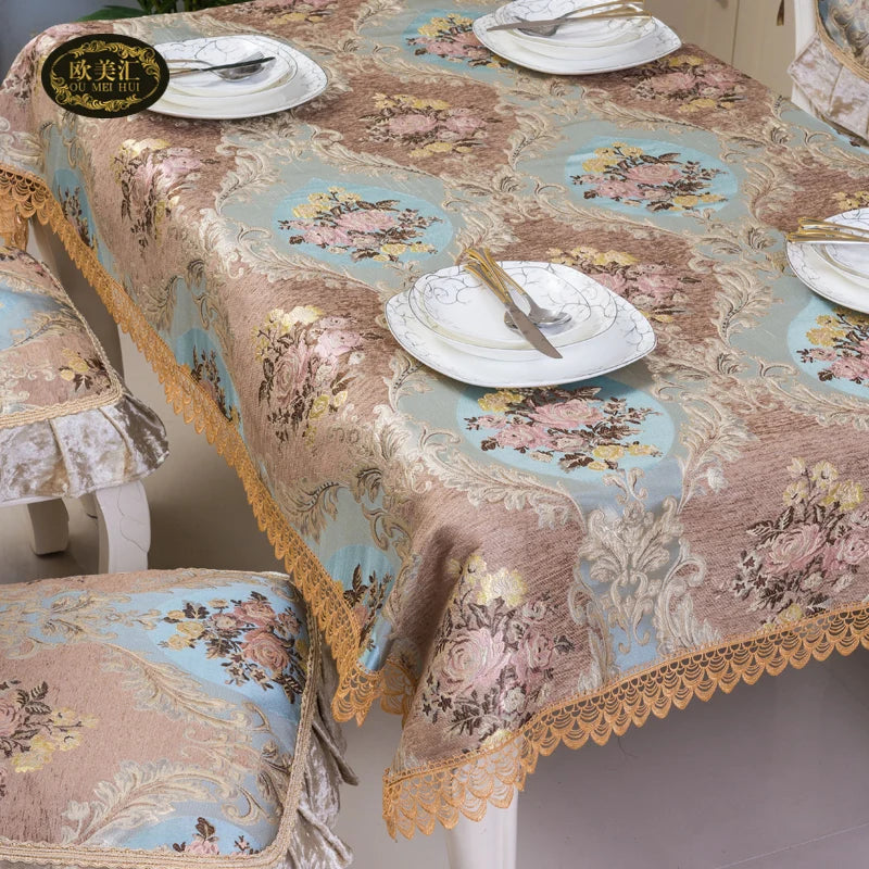 Nappe de table élégante en satin beige et bleu avec motifs floraux, ornée de dentelle dorée, accompagnée d'assiettes et de couverts raffinés.