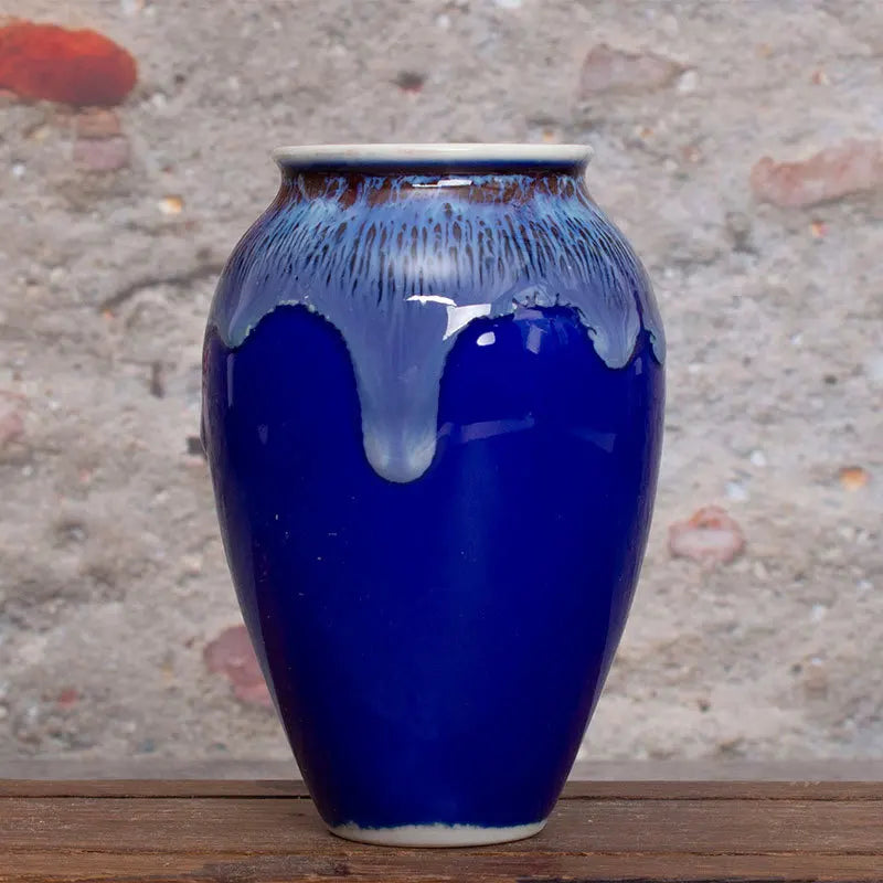 Vase en céramique bleu foncé avec des éclaboussures de glace bleue et blanche, posé sur une surface en bois.