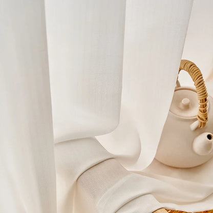 Détail du tissu du voilage blanc, délicatement posé sur le rebord d'une table avec une théière en céramique blanche