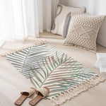 Tapis de sol blanc et beige avec motifs végétaux et franges, assorti à des coussins décoratifs dans un environnement intérieur lumineux.