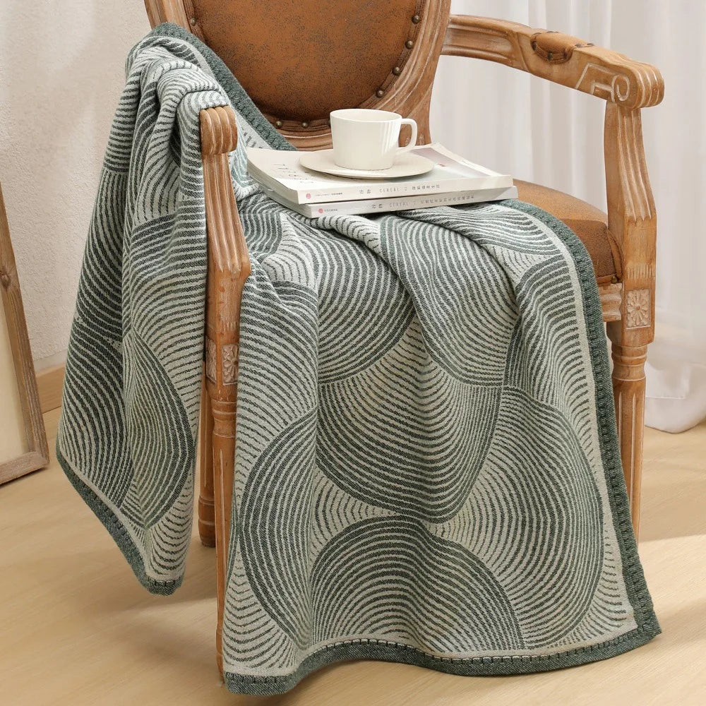 Une couverture tricotée de motifs géométriques et de rayures dans des tons de gris, disposée sur un fauteuil en bois dans un décor de pièce accueillante.