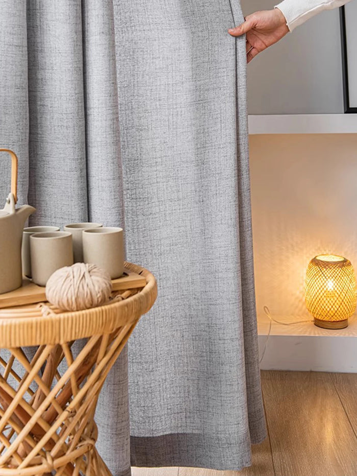 Gros plan sur un voilage gris clair tamisant, tenu à la main dans une ambiance cocooning.