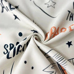 Tissu décoratif blanc avec motifs cosmiques et inscriptions stylisées en lettres noires et oranges, idéal pour les projets de couture modernes et créatifs. Parfait pour donner une touche d'originalité à votre intérieur ou pour des vêtements uniques.
