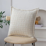 Coussin décoratif beige texturé avec un motif intéressant, posé sur un fauteuil en métal dans un intérieur moderne.
