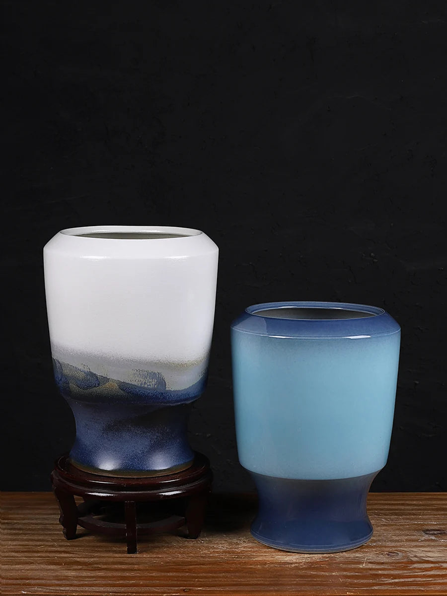 Deux vases décoratifs de différentes tailles et couleurs, posés sur un support en bois, créent une composition esthétique et minimaliste dans un décor sombre.