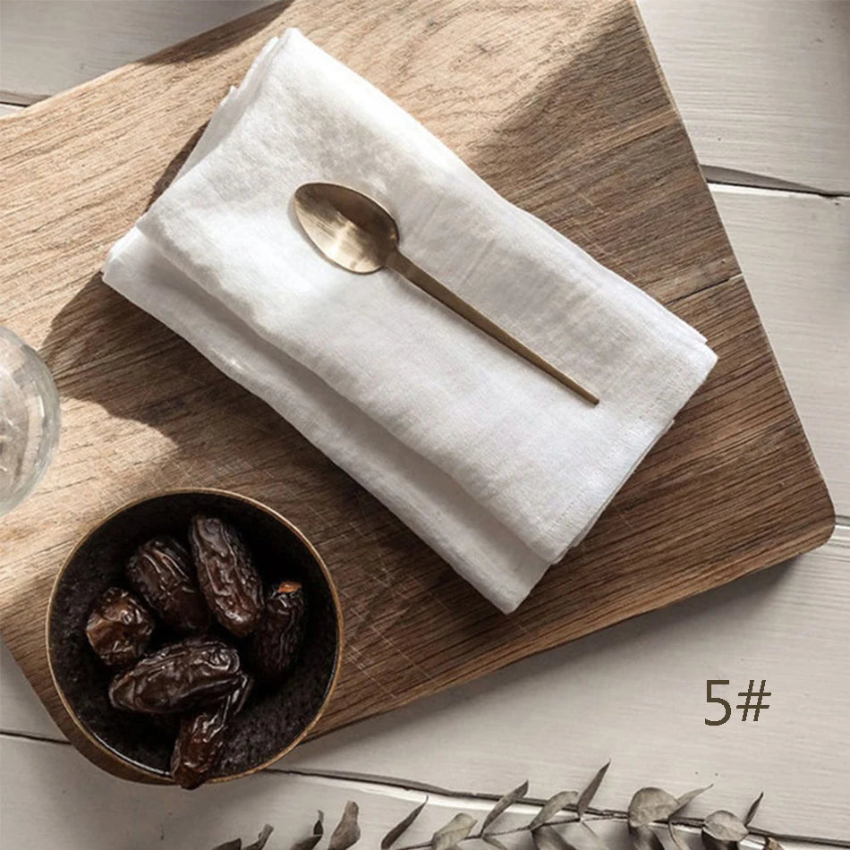 Une serviette en lin blanche, une cuillère en métal doré et un bol contenant des dattes sur une planche de bois.