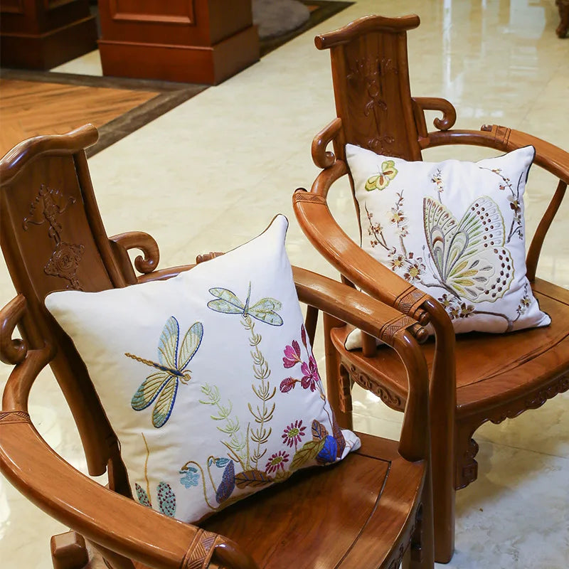 Deux chaises en bois sculpté avec des coussins décoratifs aux motifs de papillons et de fleurs, dans un décor d'intérieur avec un sol en carrelage.