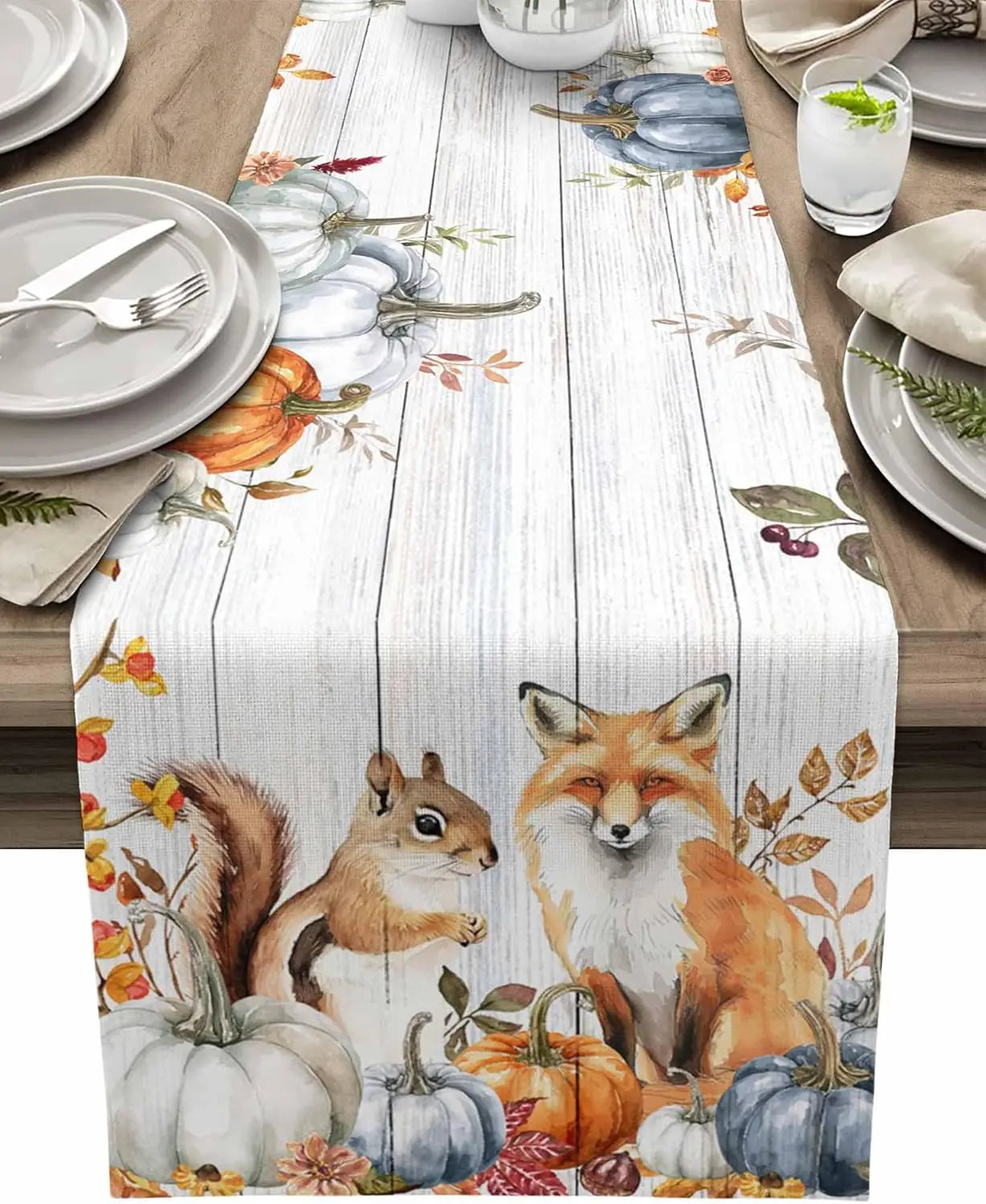 Sur la table de salle à manger, on voit une belle nappe avec des motifs de renards, d'écureuils et de citrouilles d'automne, créant une ambiance chaleureuse et automnale.