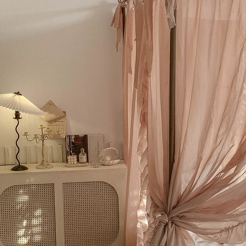 Un intérieur élégant et douillet avec des rideaux rose pâle, des objets décoratifs sur un meuble et une lampe de table vintage, créant une atmosphère chaleureuse et apaisante.