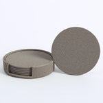 Des sous-verres ronds en gris foncé, empilés et présentés sur fond blanc.