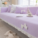 Un intérieur lumineux et élégant avec des coussins et une couverture violets ornés de nœuds blancs, créant une ambiance apaisante et féminine dans cette pièce.