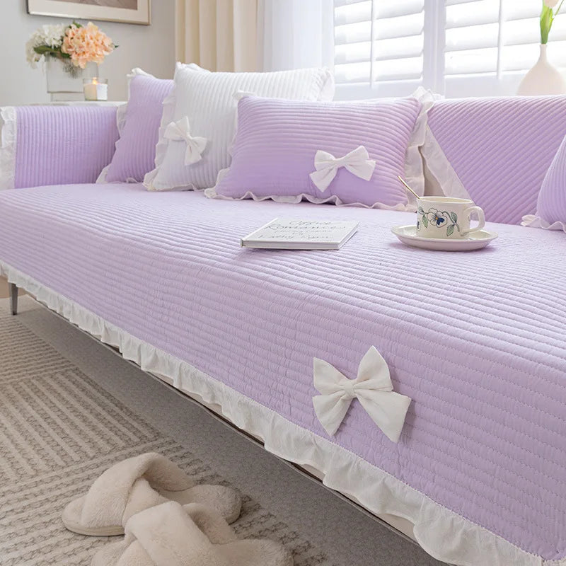 Un intérieur lumineux et élégant avec des coussins et une couverture violets ornés de nœuds blancs, créant une ambiance apaisante et féminine dans cette pièce.