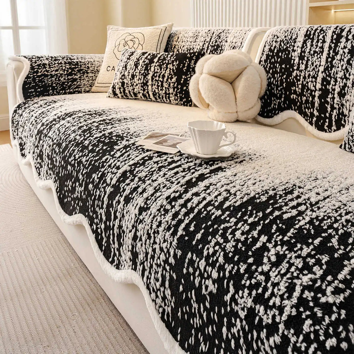 Couverture de sofa monochromatique avec motif floral en noir et blanc, avec un oreiller douillet et une tasse sur la table basse, créant une ambiance cosy et apaisante.