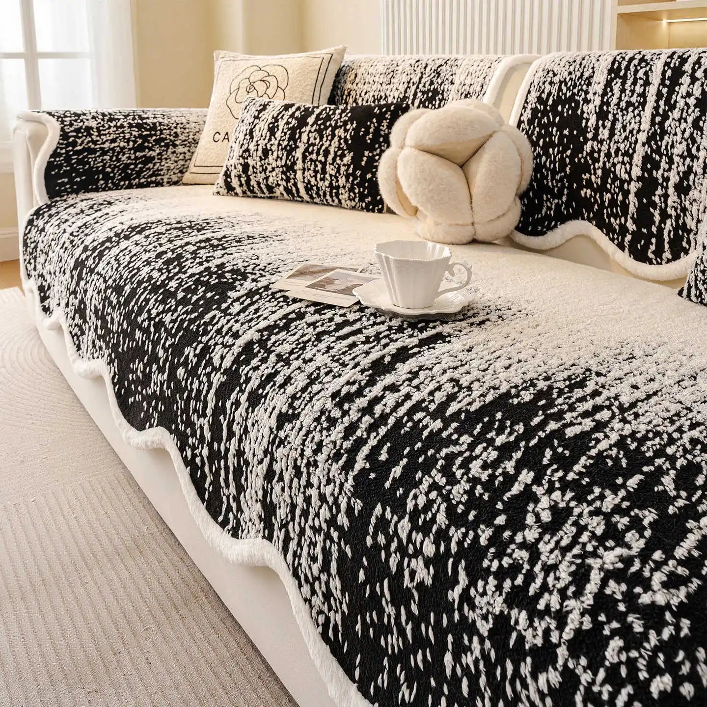 Couverture de sofa monochromatique avec motif floral en noir et blanc, avec un oreiller douillet et une tasse sur la table basse, créant une ambiance cosy et apaisante.