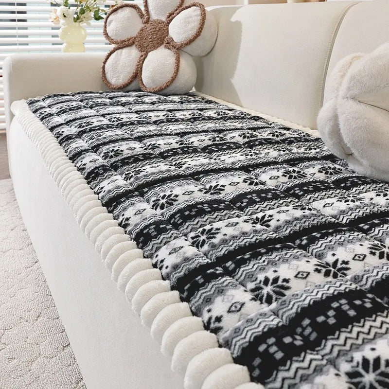 Couverture de lit moelleuse avec un motif floral et géométrique en noir et blanc, sur un canapé beige avec un coussin en forme de fleur marron.