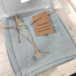 Serviettes en lin pur de couleur grise sous emballage transparent, avec une étiquette indiquant qu'il s'agit de serviettes en lin 100% pur.