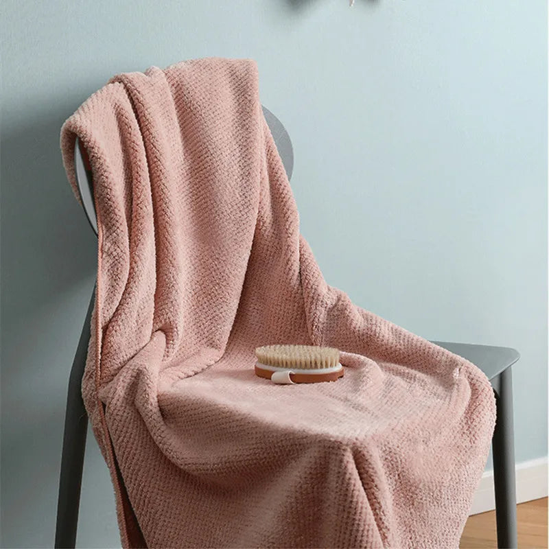Une couverture rose pastel, douillette et accueillante, posée sur une chaise, avec une brosse en bois, invitant à une pause détente.