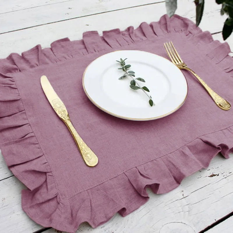 Une assiette blanche avec une feuille verte déposée sur une nappe de table rose volantée, avec des couverts dorés posés autour.