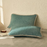 Deux oreillers décoratifs en tricot turquoise avec bordure beige posés sur une surface blanche.