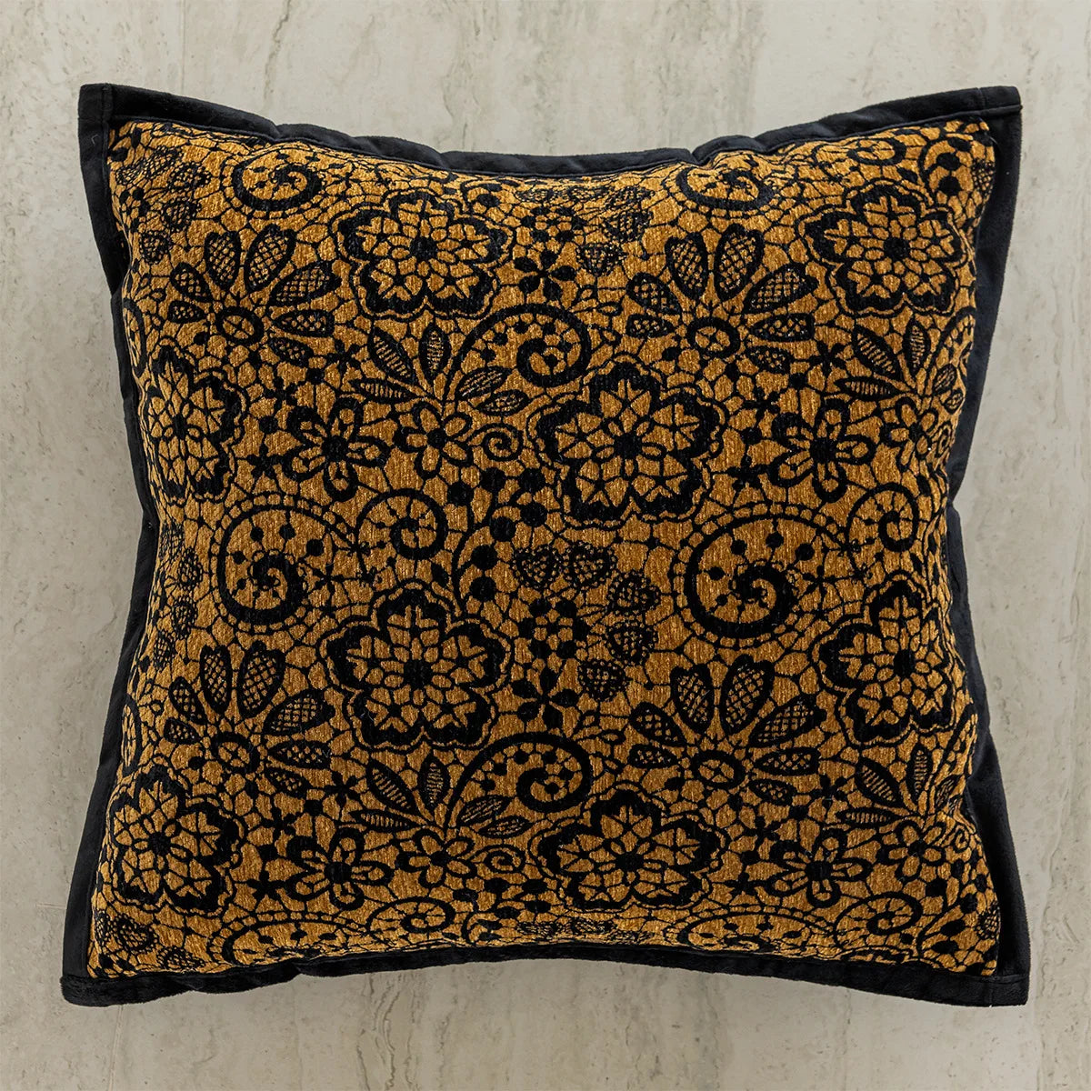 Coussin décoratif avec motif floral doré et noir sur fond blanc cassé.