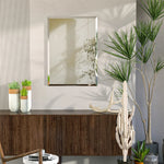 Cette image décorative montre un cadre mural blanc encadré sur un meuble en bois sombre, orné de plantes vertes, de sculptures et d'accessoires décoratifs qui créent une ambiance zen et naturelle.