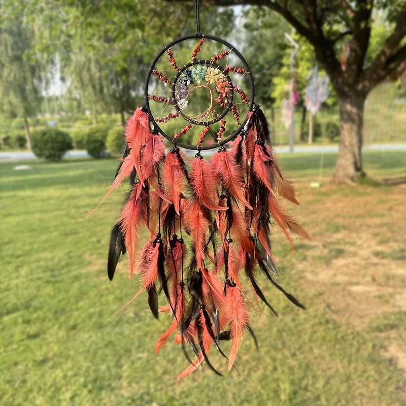 Magnifique attrape-rêves suspendu dans un parc verdoyant, orné de plumes rouges et vertes, de perles et de pierres, créant une œuvre d'art naturelle captivante.