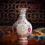 Vase en porcelaine décoré de motifs floraux colorés et de motifs ajourés sur un fond sombre.