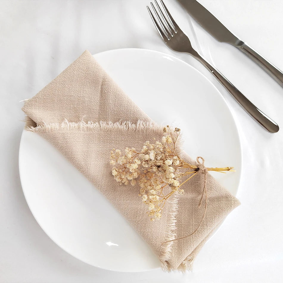 Une assiette blanche avec une serviette de table en lin beige et de délicates fleurs séchées, accompagnée de couverts en métal.