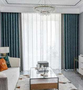 Salon moderne avec rideaux élégants, combinant des draperies bleu marine et voilages blancs. Le salon est aménagé avec un canapé confortable, une table basse en verre, et des éléments décoratifs raffinés. Une ambiance lumineuse et sophistiquée est accentuée par un lustre décoratif suspendu. Parfait pour une décoration intérieure élégante et contemporaine.