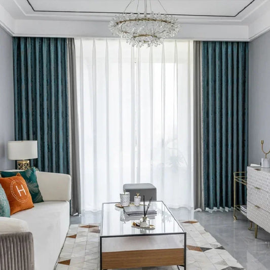 Salon moderne avec rideaux élégants, combinant des draperies bleu marine et voilages blancs. Le salon est aménagé avec un canapé confortable, une table basse en verre, et des éléments décoratifs raffinés. Une ambiance lumineuse et sophistiquée est accentuée par un lustre décoratif suspendu. Parfait pour une décoration intérieure élégante et contemporaine.