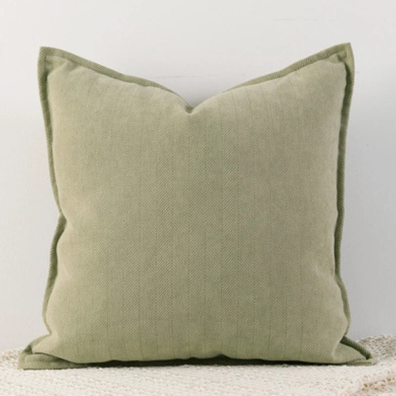 Un coussin décoratif vert olive avec un motif texturé en chevrons, posé sur une surface blanche, créant une ambiance douce et apaisante.