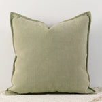 Un coussin décoratif vert olive avec un motif texturé en chevrons, posé sur une surface blanche, créant une ambiance douce et apaisante.