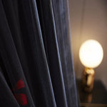 Rideau sombre aux motifs de fleurs rouges, avec une lampe en arrière-plan dans une ambiance feutrée et tamisée.
