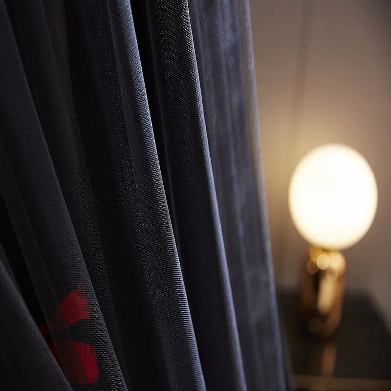 Rideau sombre aux motifs de fleurs rouges, avec une lampe en arrière-plan dans une ambiance feutrée et tamisée.