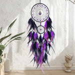 Un attrapeur de rêves décoratif aux plumes violettes et noires, suspendu au mur sur un fond clair.