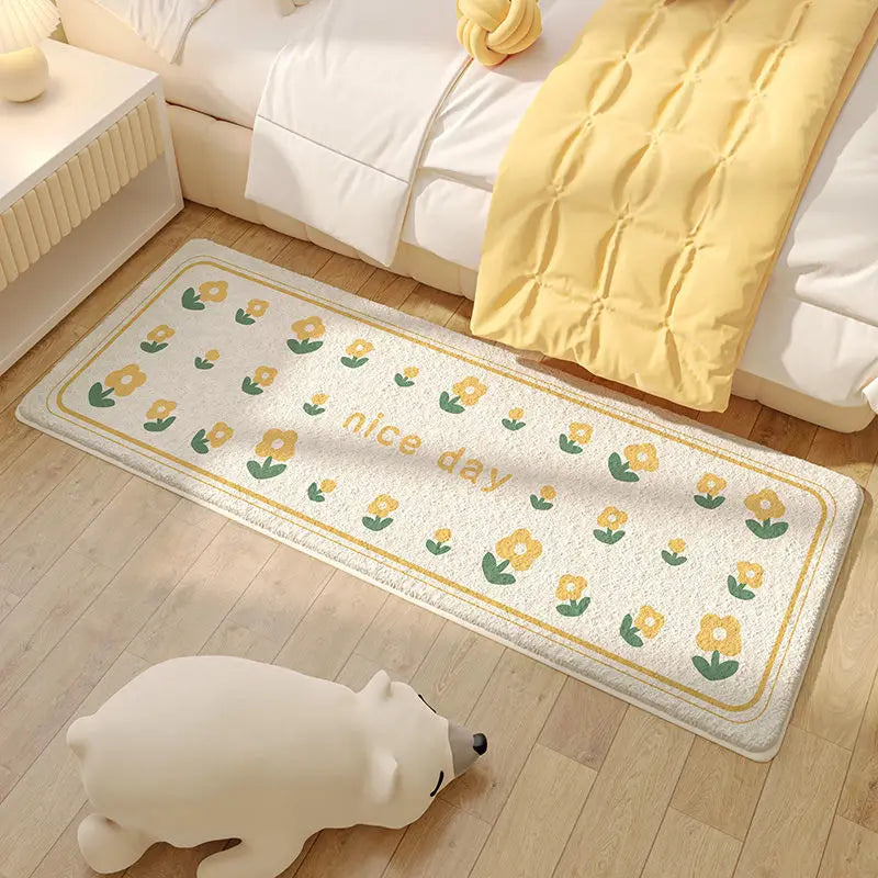 Un tapis de sol avec un motif de fleurs jaunes et vertes, sur un sol en bois clair, avec un ours en peluche blanc à côté.