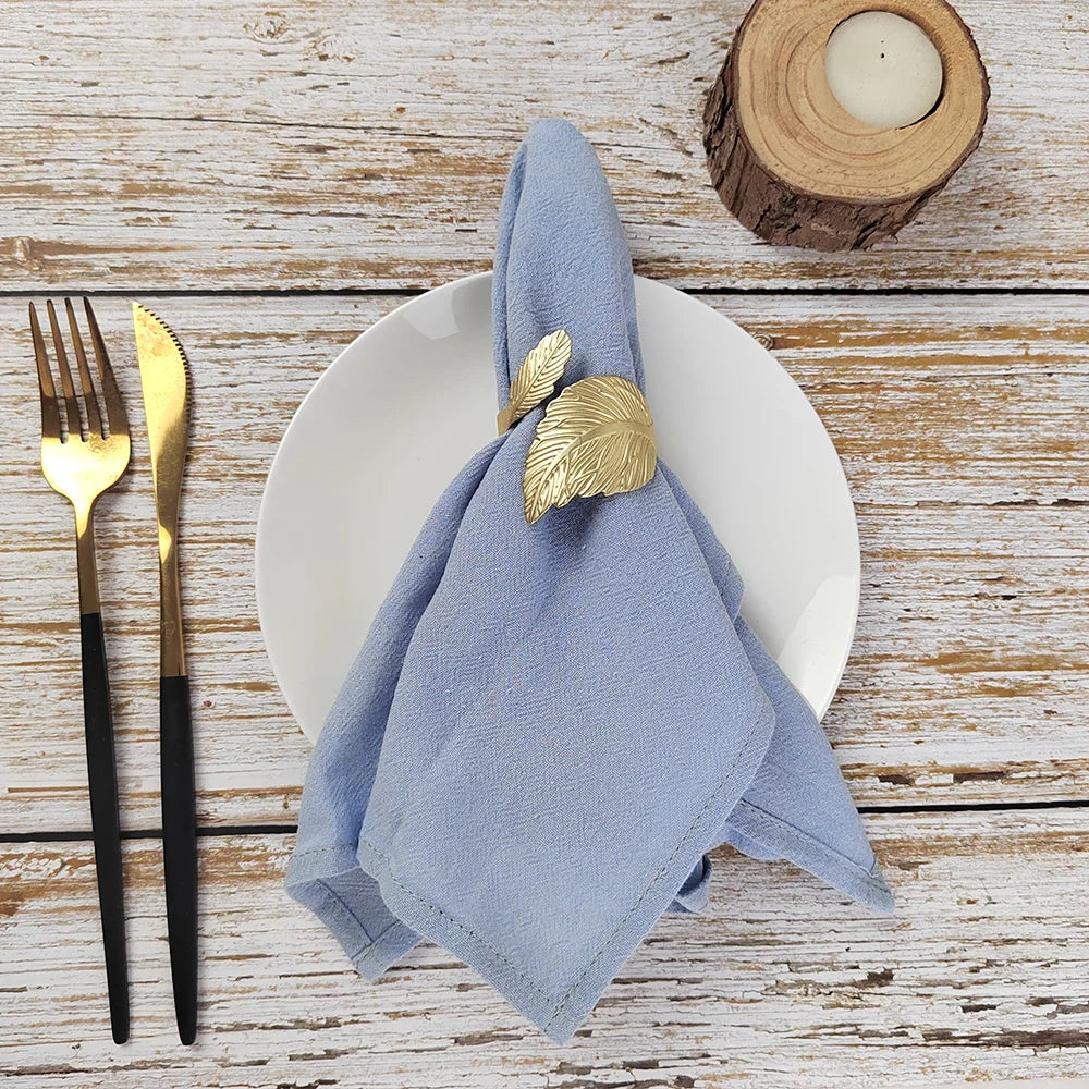 Une table de cuisine aux couleurs naturelles, avec une serviette grise enroulée autour d'un support en bois, une bougie allumée et des ustensiles de cuisine dorés.