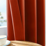 Gros plan sur un rideau drapé orange brûlé avec texture en tissu épais, partiellement ouvert, laissant entrevoir un paysage tropical à l'extérieur.