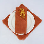 Une serviette en lin de couleur ocre avec un petit bouquet de fleurs séchées posé sur une assiette blanche représente une décoration de table élégante et automnale.