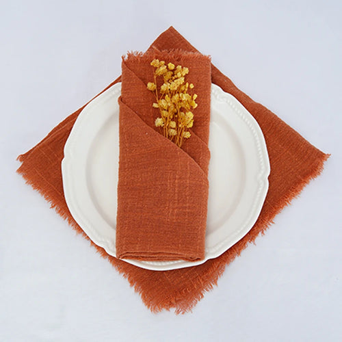Une serviette en lin de couleur ocre avec un petit bouquet de fleurs séchées posé sur une assiette blanche représente une décoration de table élégante et automnale.
