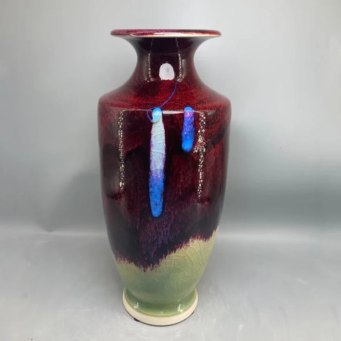 Un vase décoratif de couleur bordeaux et verte avec des touches de bleu, offrant un design unique et artistique.