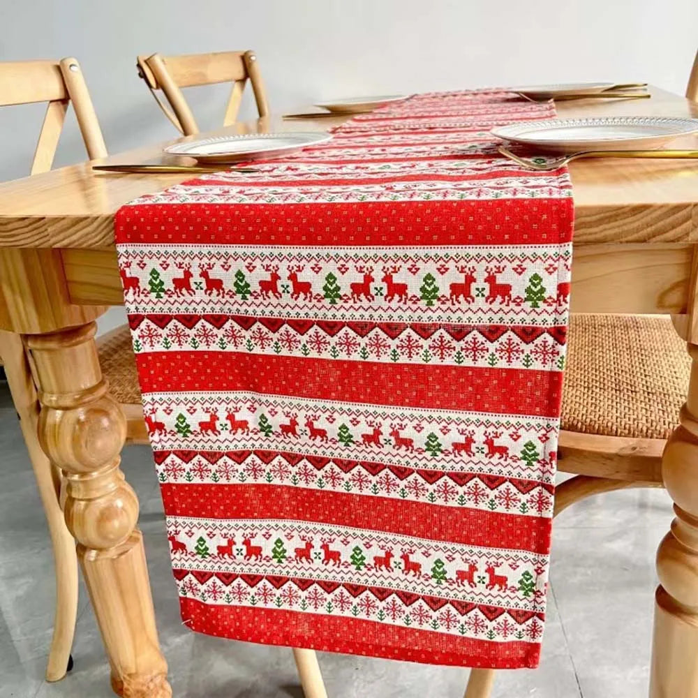 Un chemin de table de Noël rouge et blanc, orné de motifs de rennes et de flocons de neige, décorant une table en bois.