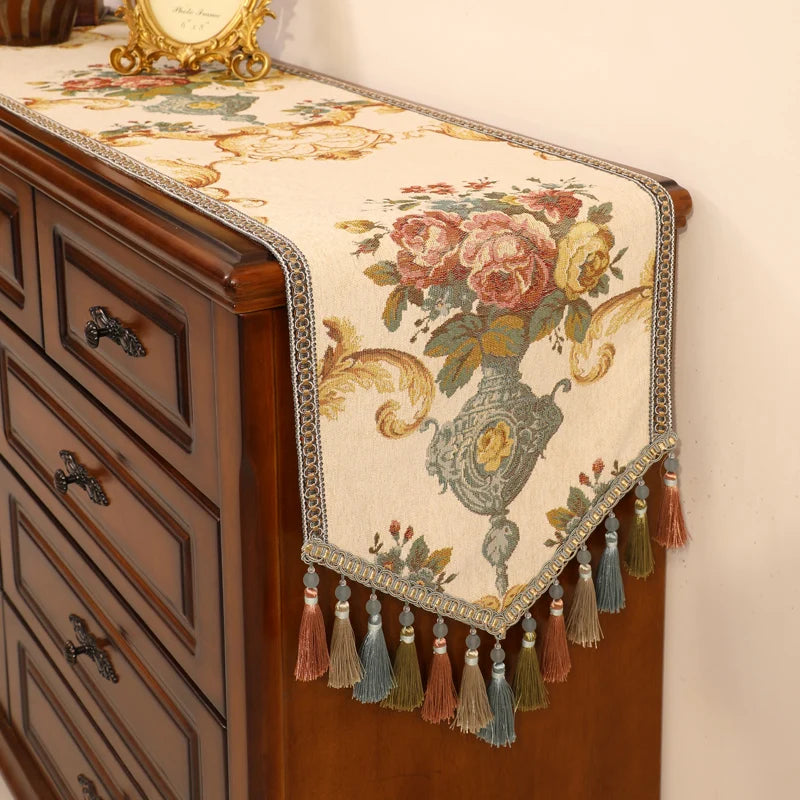 Une table basse en bois décorative avec un chemin de table en tapisserie vintage orné de fleurs colorées et de tassels.