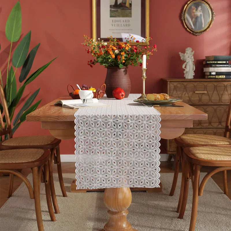 Cette image montre une table dressée dans une pièce élégante avec un bouquet de fleurs colorées, une bougie, des fruits et d'autres accessoires décoratifs.