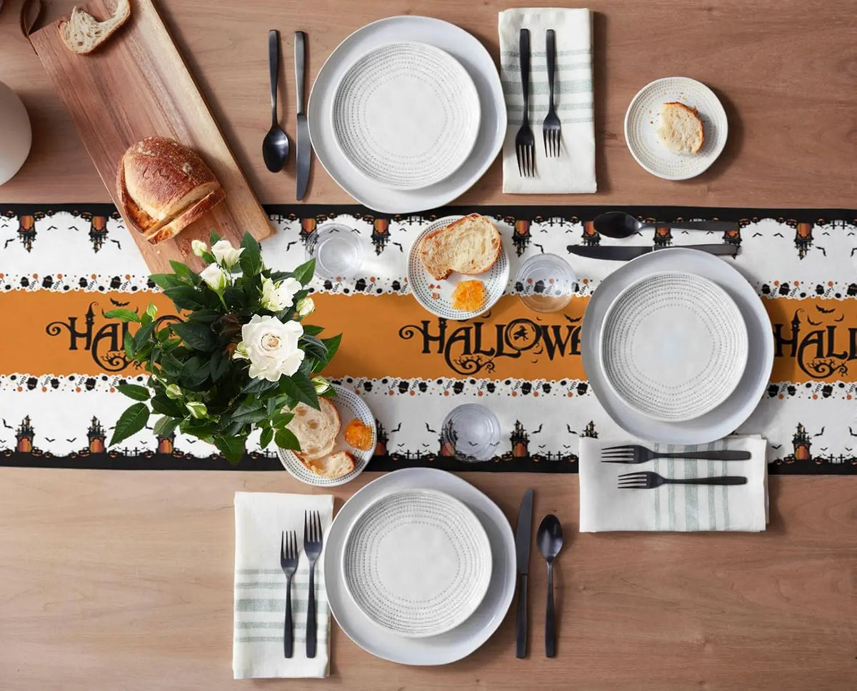 Une table de fête de Halloween joliment dressée avec des assiettes, des couverts, des fleurs et une nappe aux motifs effrayants.