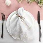 Un service de table élégant avec une serviette blanche attachée avec de la ficelle et des fleurs sur un fond rose pâle.