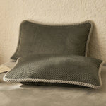 Deux oreillers carrés gris foncé avec bordure blanche se trouvent sur un fond beige clair.