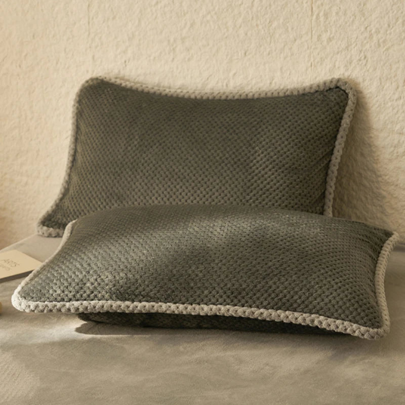 Deux oreillers carrés gris foncé avec bordure blanche se trouvent sur un fond beige clair.